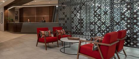 A modern reception area with a reception desk, red upholstered chairs, a round coffee table, and a decorative wall with a geometric pattern.