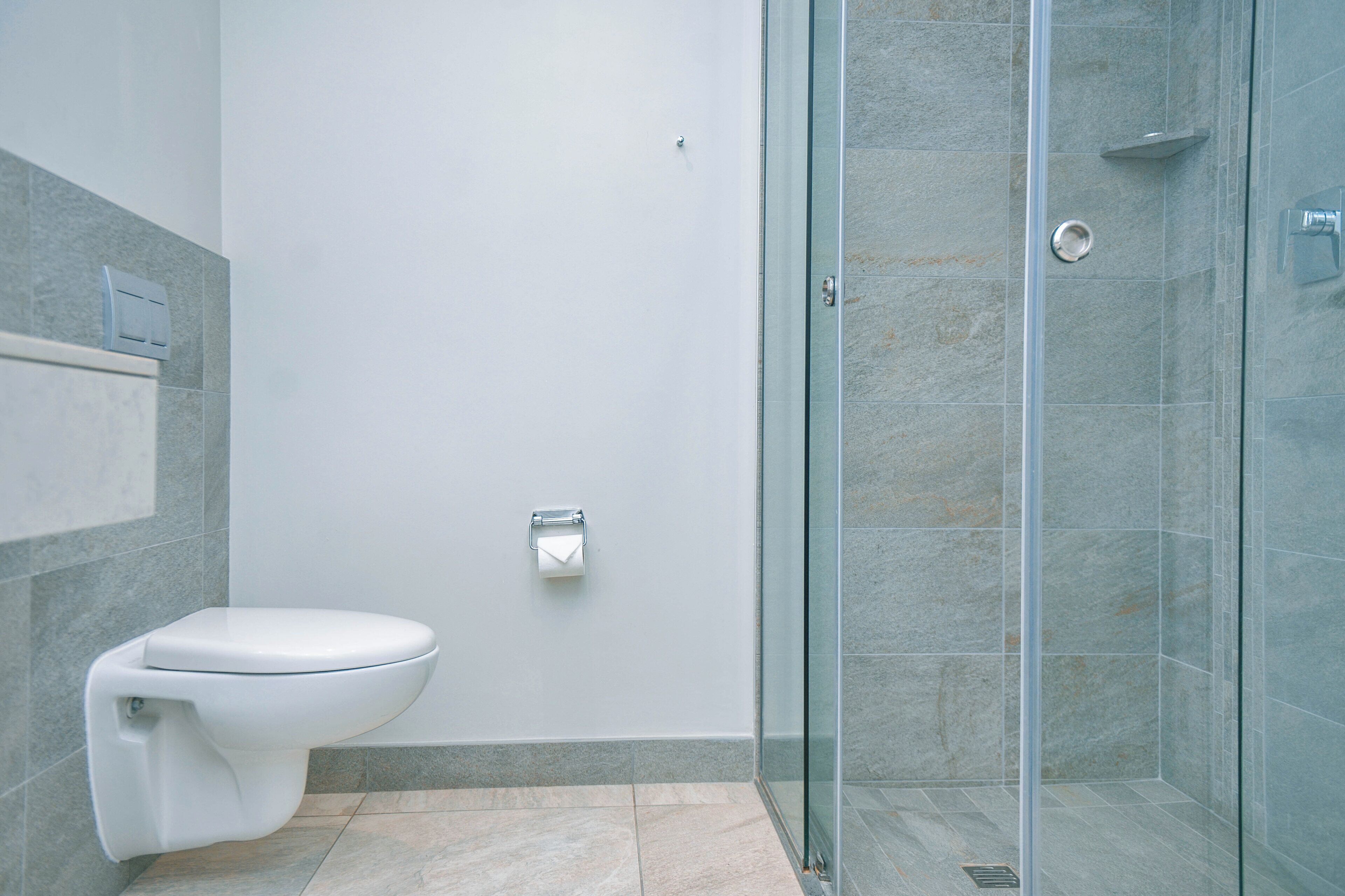A modern bathroom with a toilet, a glass shower enclosure, and a marble-tiled floor.