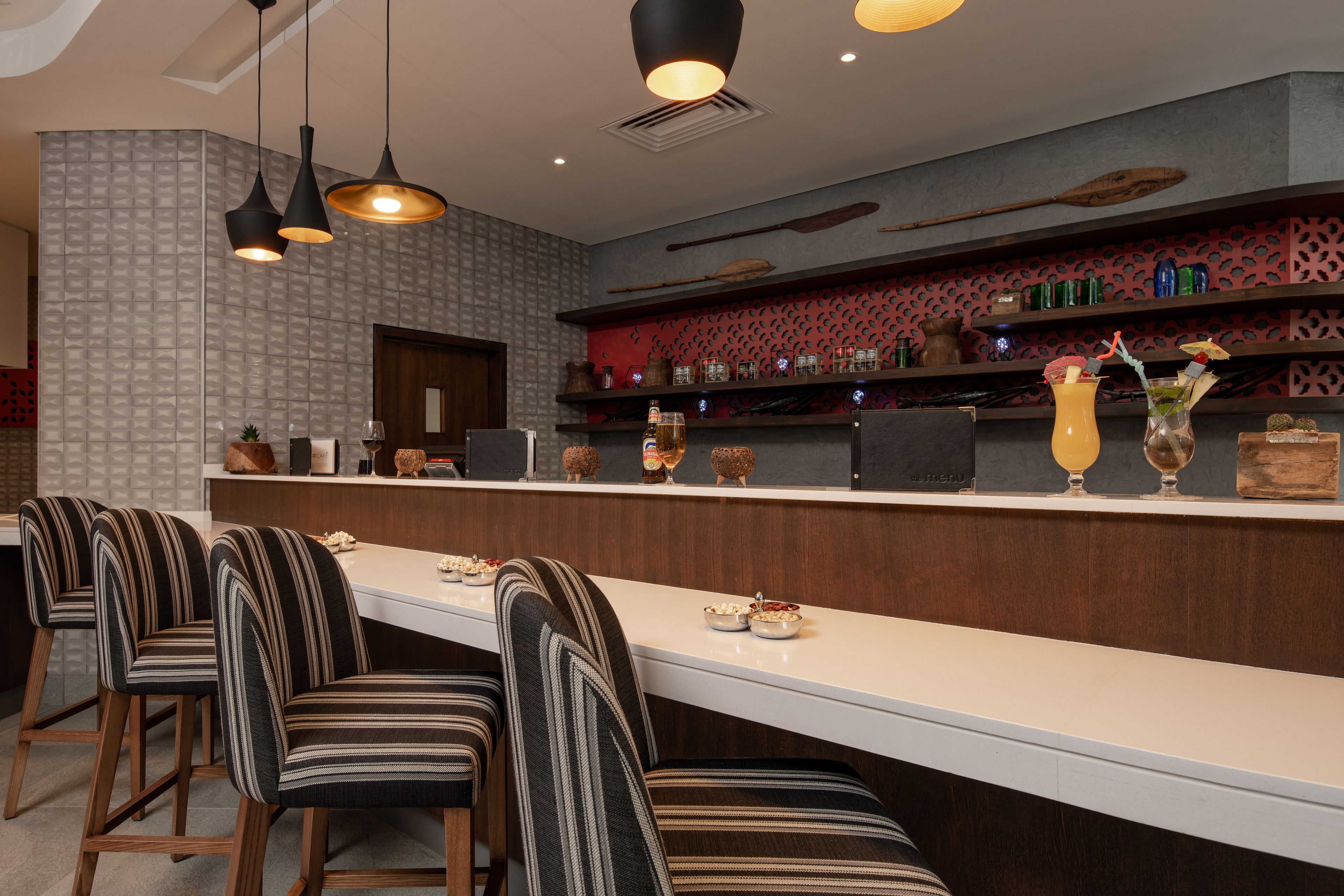 A modern bar area with striped chairs, a long counter, and decorative items like vases and bottles.