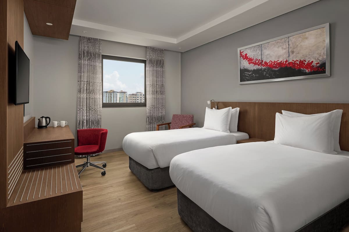 Une chambre d’hôtel avec deux lits, un bureau, une chaise, une télévision et une fenêtre donnant sur la ville.