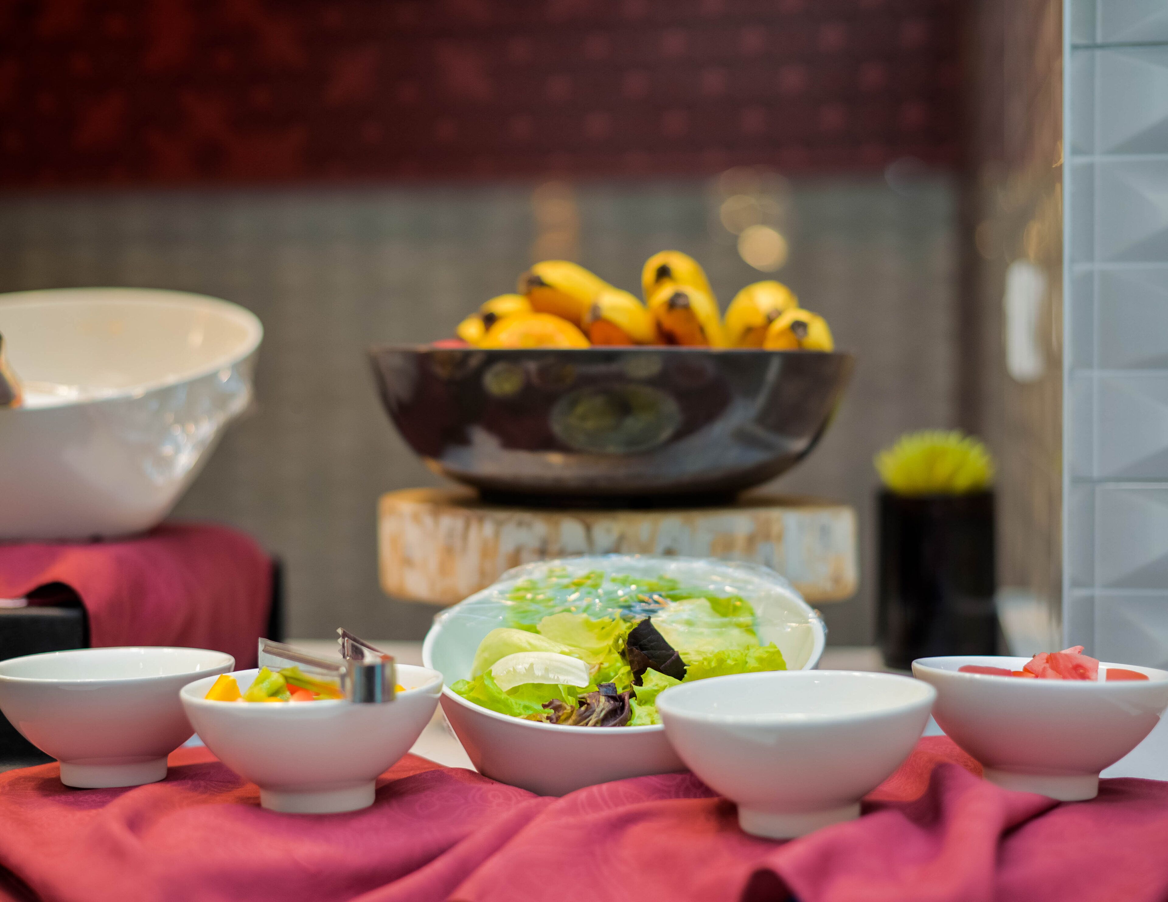 Een tafel met diverse kommen vol eten, een kom bananen en een kom salade.