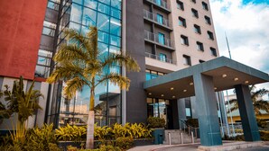 A modern hotel with a glass facade, a covered entrance, and a palm tree in the foreground. - Crowne Plaza Dar es Salaam by IHG (Dar es Salaam)