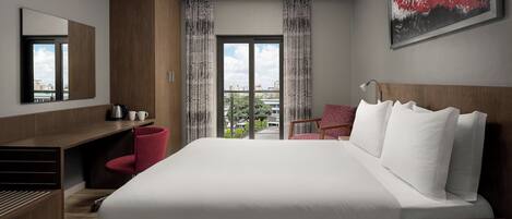 Habitación de hotel moderna con una cama grande, un escritorio, una silla y vistas a la ciudad desde la ventana.
