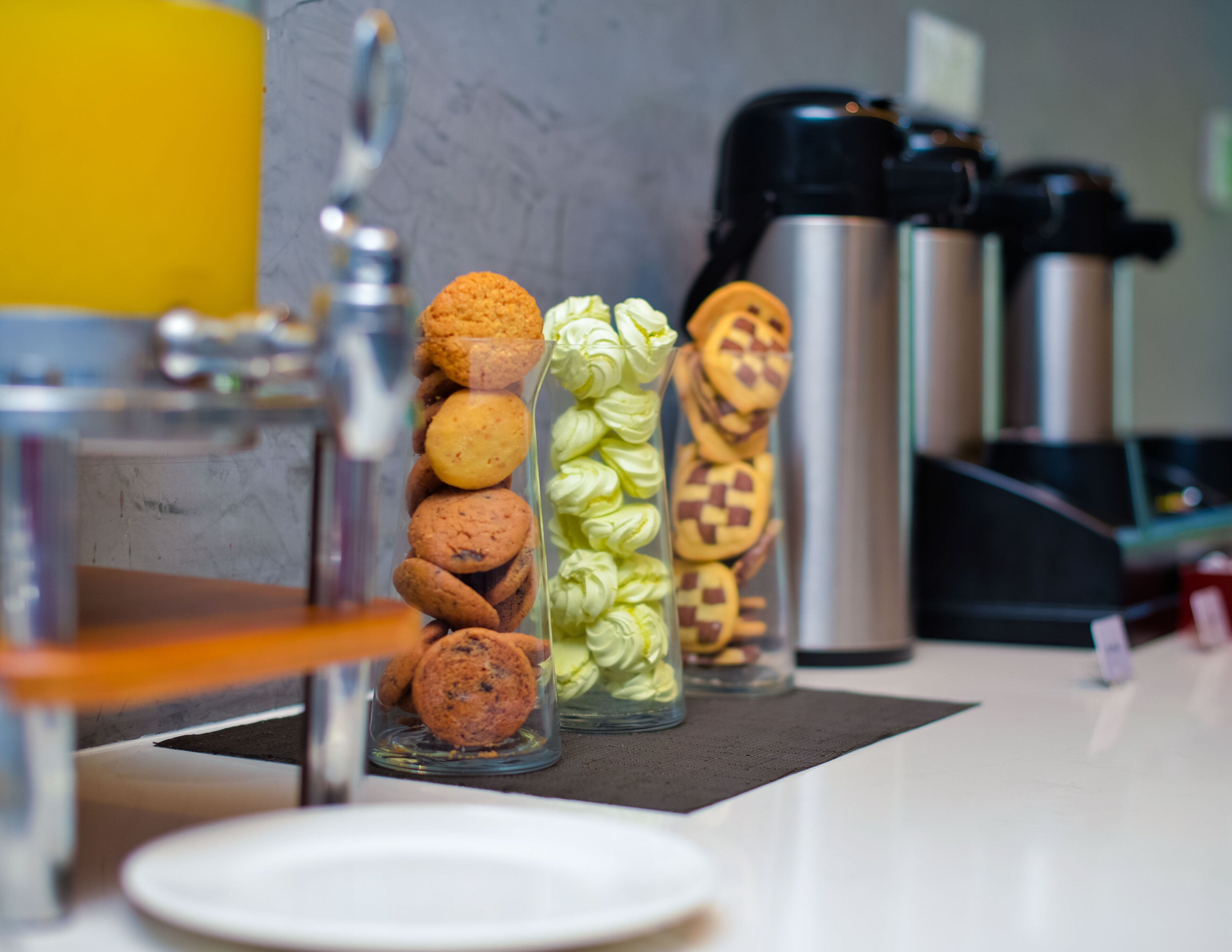 A kitchen counter with a coffee maker, a kettle, and jars of cookies and pastries.