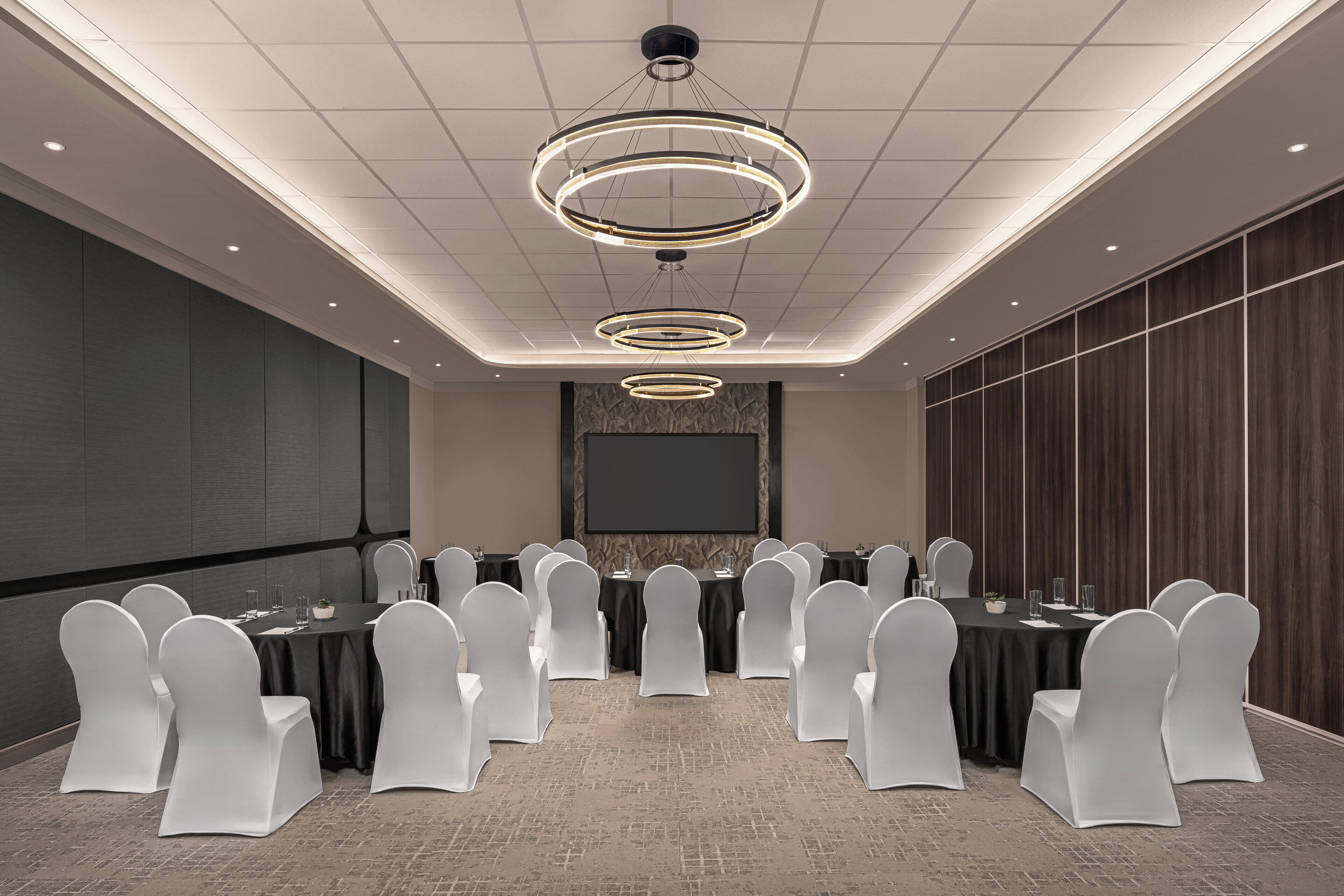 A conference room with a large screen, multiple tables, and white chairs.
