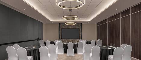 A conference room with a large screen, multiple tables, and white chairs.