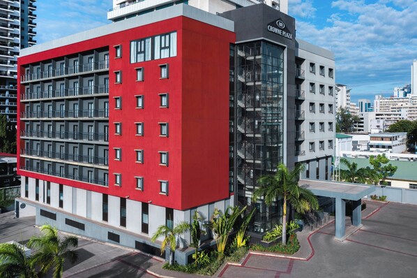 A modern hotel with a red and grey facade, multiple balconies, and a glass entrance.