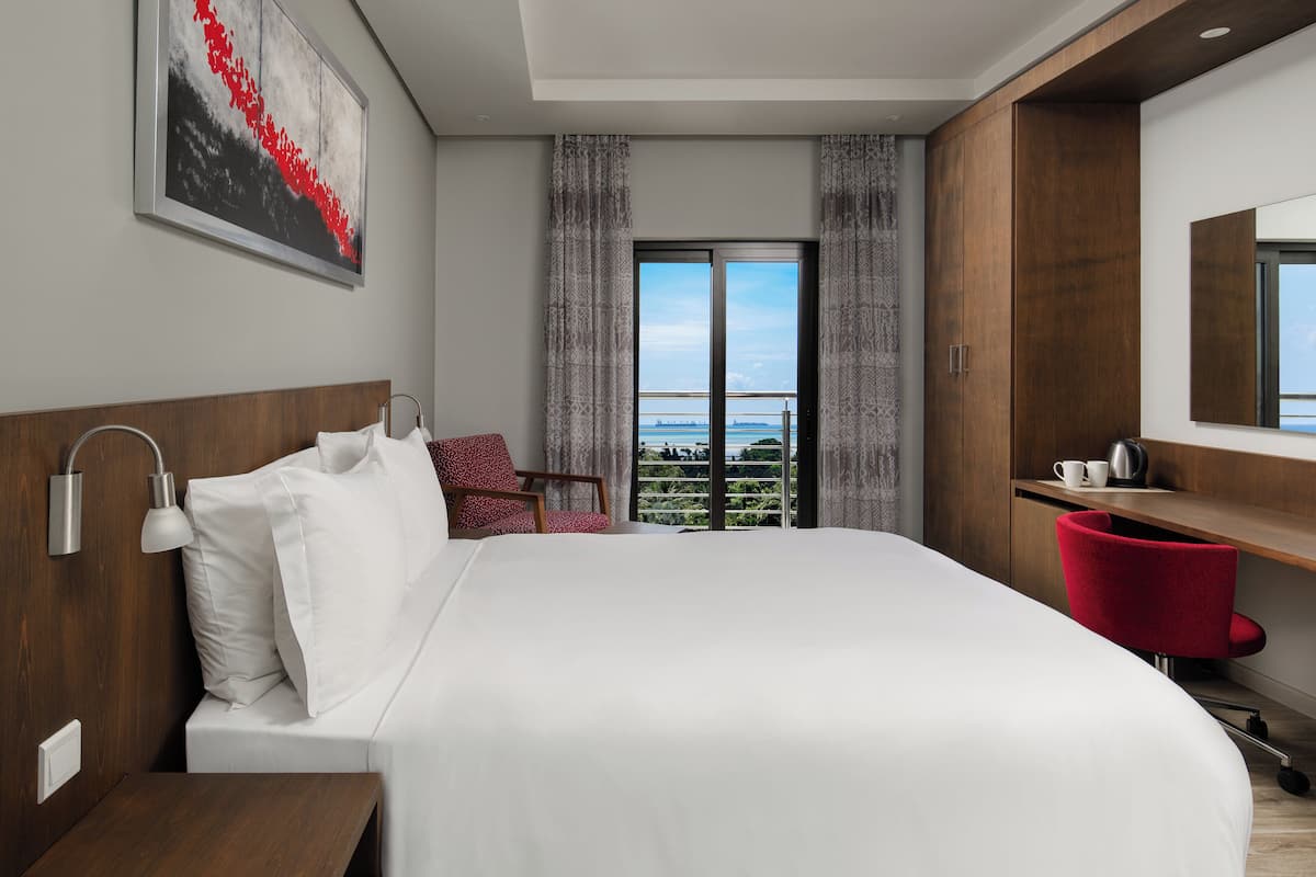 Une chambre d’hôtel moderne, dotée d’un grand lit, d’un bureau, d’une chaise et offrant une vue sur la ville grâce à une grande fenêtre.