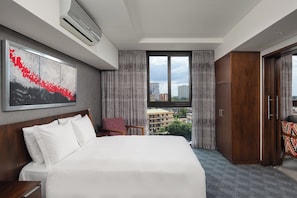 Quarto de hotel com uma cama grande, uma escrivaninha, uma cadeira, um guarda-roupa e uma janela com vista para a cidade.