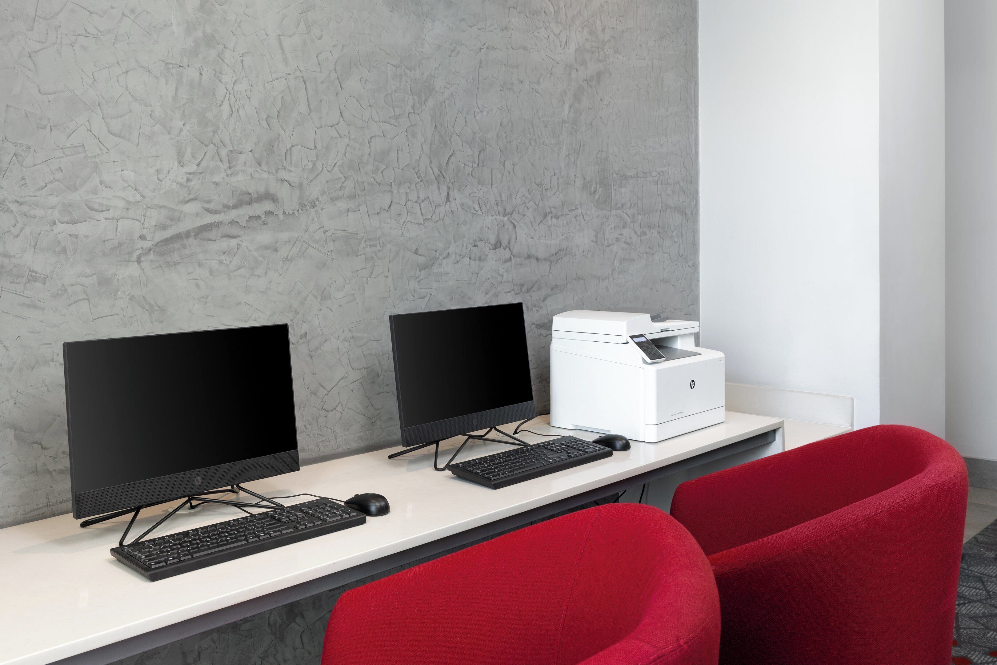 A modern office desk with two monitors, a keyboard, and a printer.