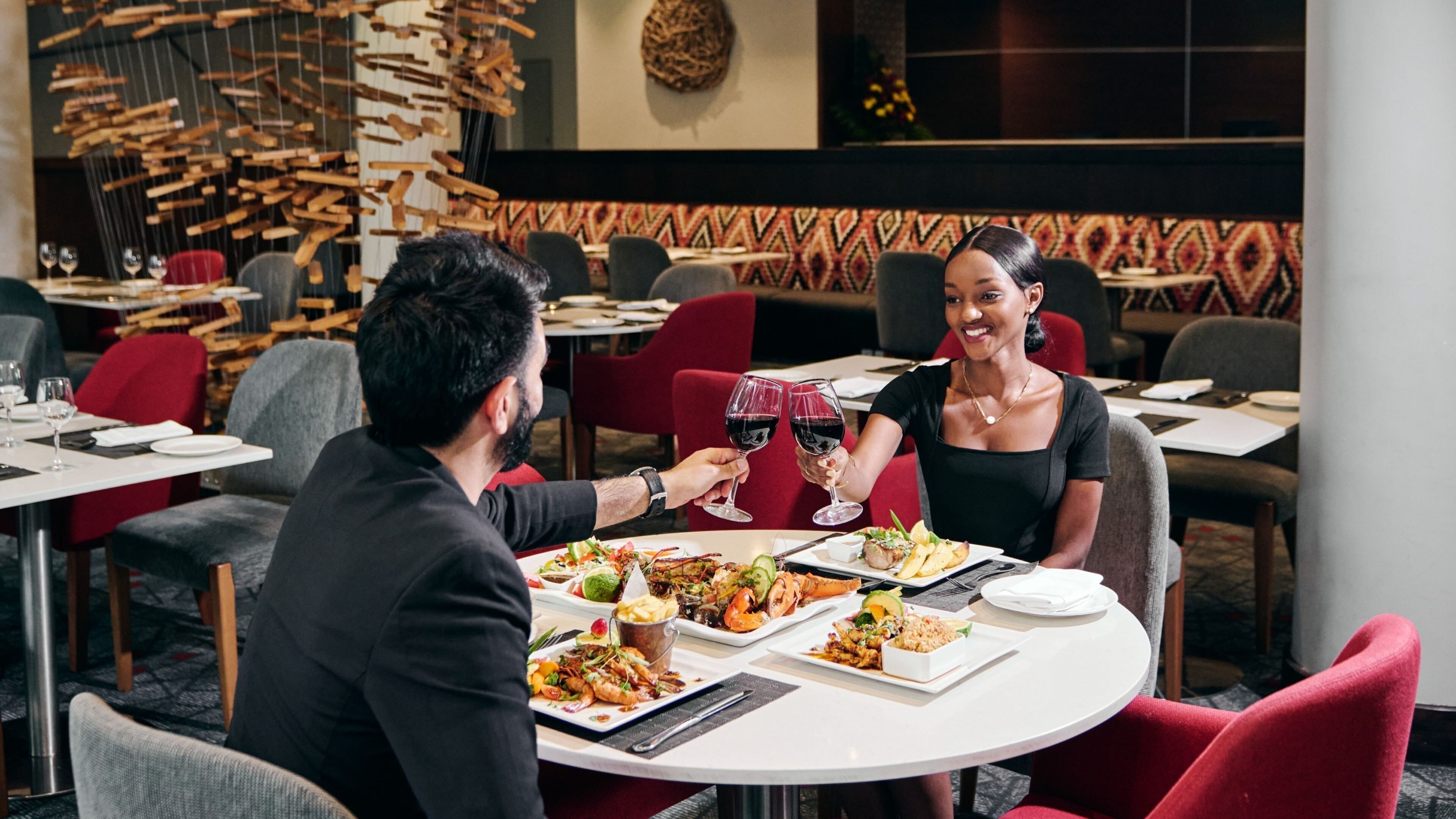 A restaurant setting with a round table, red chairs, and a variety of dishes including seafood and salads.