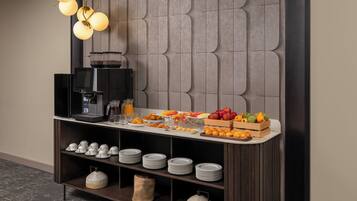 Un bufé de desayuno con una máquina de café, fruta y platos apilados.