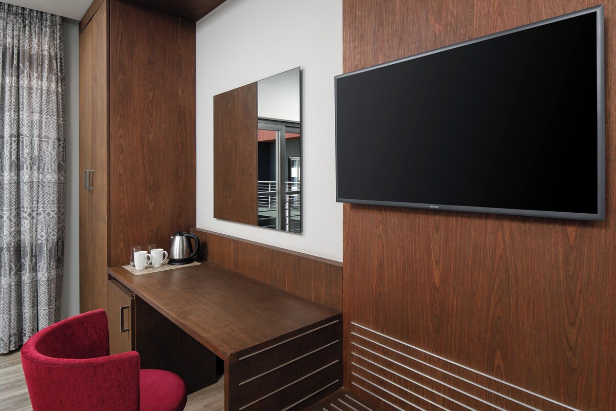Une chambre d’hôtel avec un bureau en bois, une chaise rouge, une télévision et un miroir.