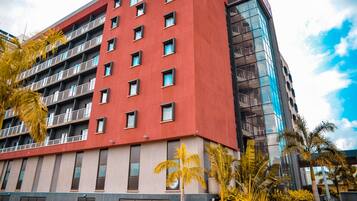A multi-story hotel with a red facade, balconies, and a glass building adjacent to it.