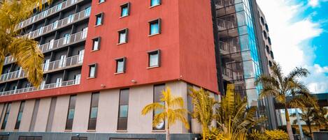 A multi-story hotel with a red facade, balconies, and a glass building adjacent to it.