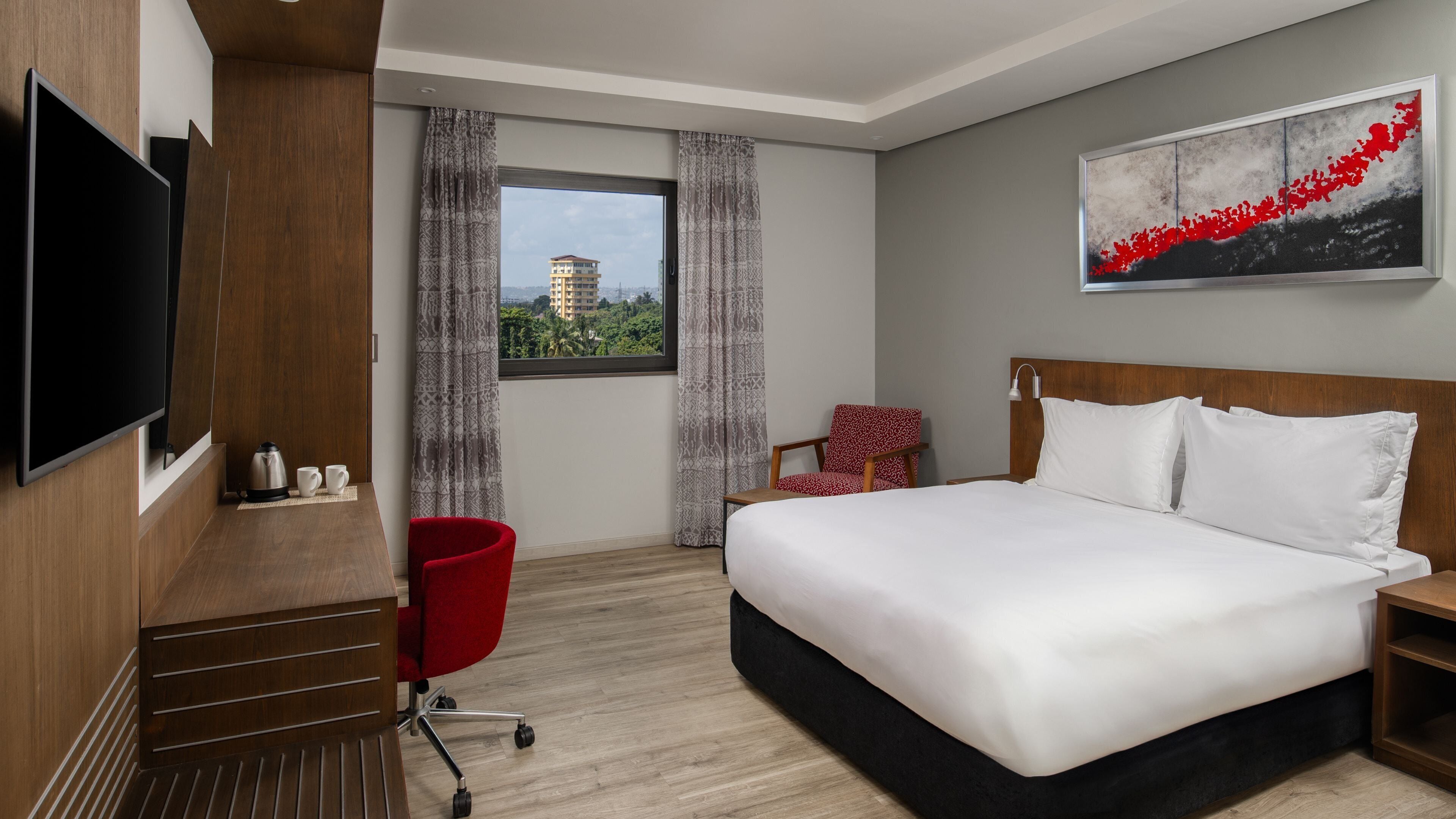 A hotel room with a large bed, a TV, a coffee maker, and a view of a cityscape.