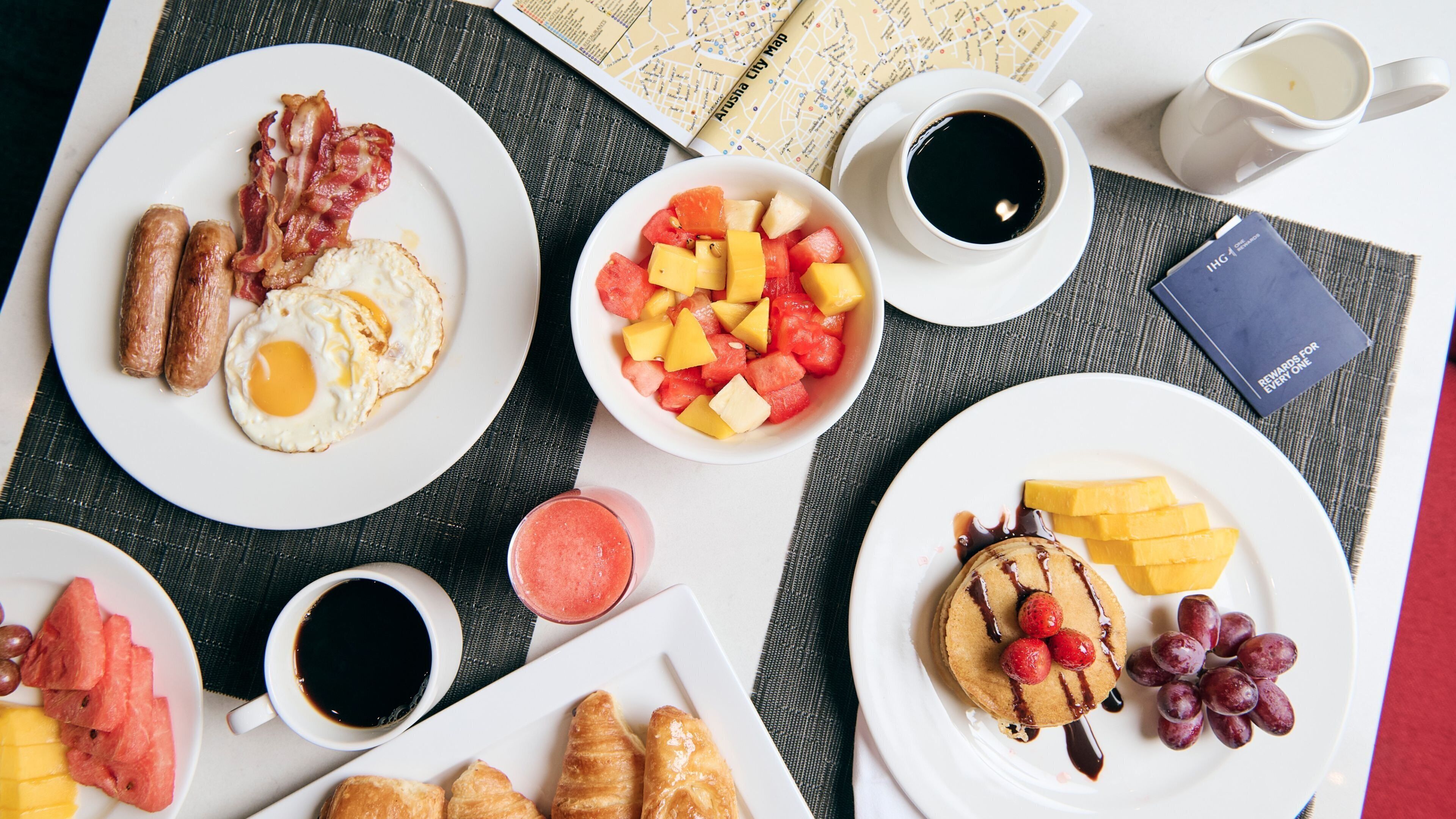 A breakfast setting with plates of food, including eggs, sausages, and fruit, along with cups of coffee and juice.