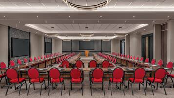 Un salón de conferencias con mesas largas, sillas rojas y una pantalla grande.