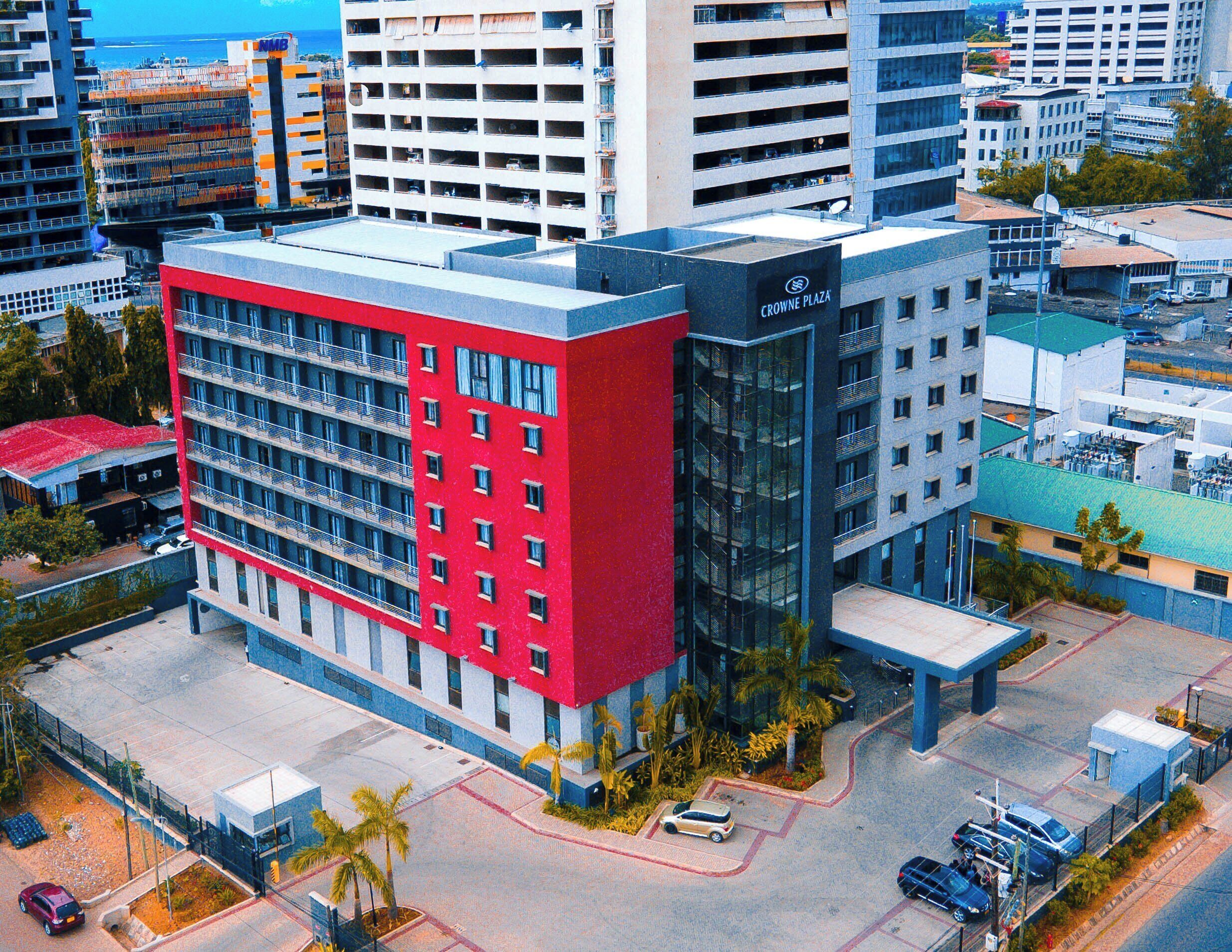 Um edifício de vários andares com fachada vermelha, entrada de vidro e estacionamento.