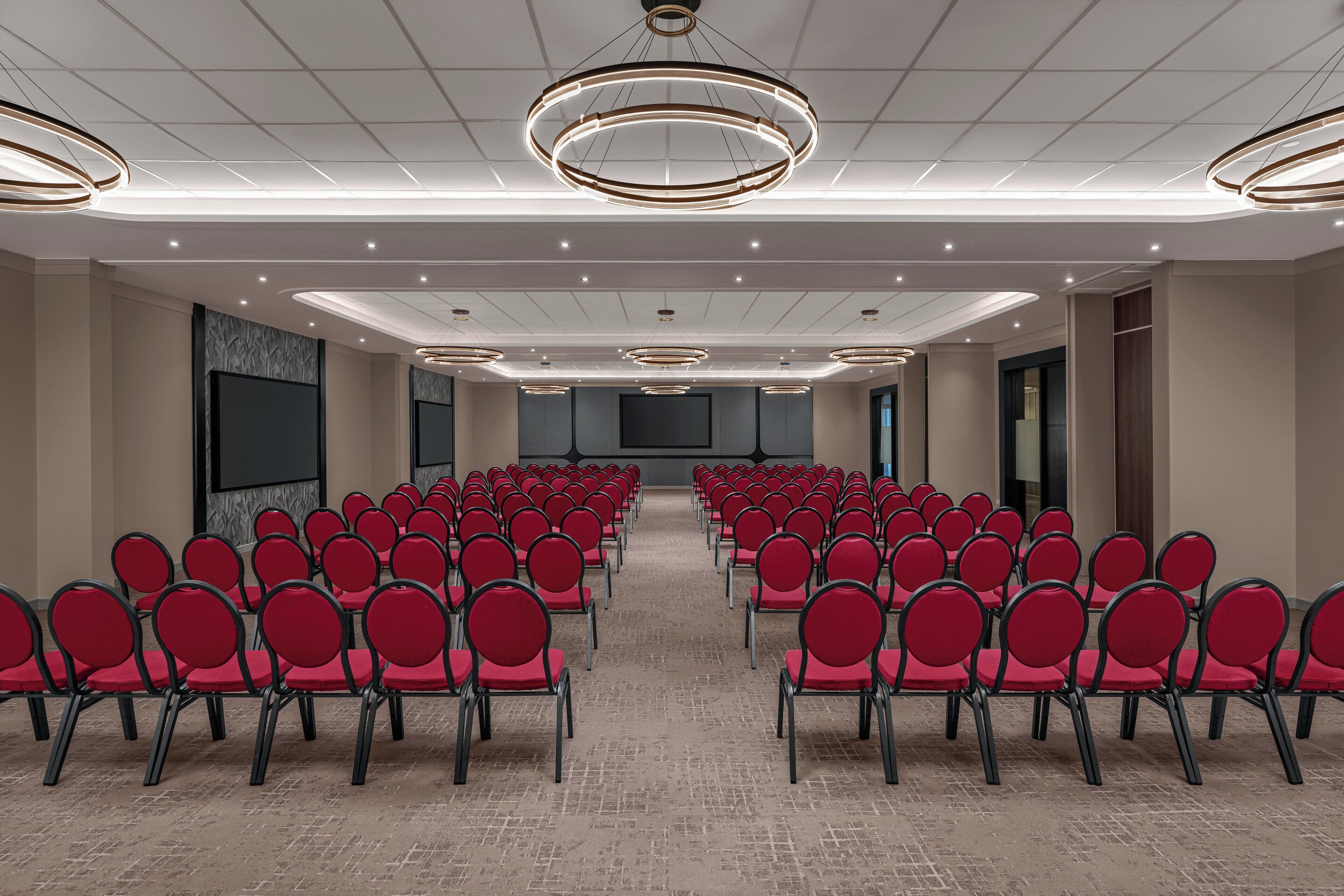 A conference room with rows of red chairs, a tiled ceiling, and recessed lighting.
