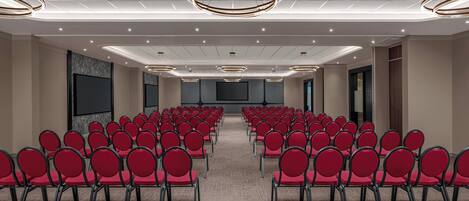 A conference room with rows of red chairs, a tiled ceiling, and recessed lighting.