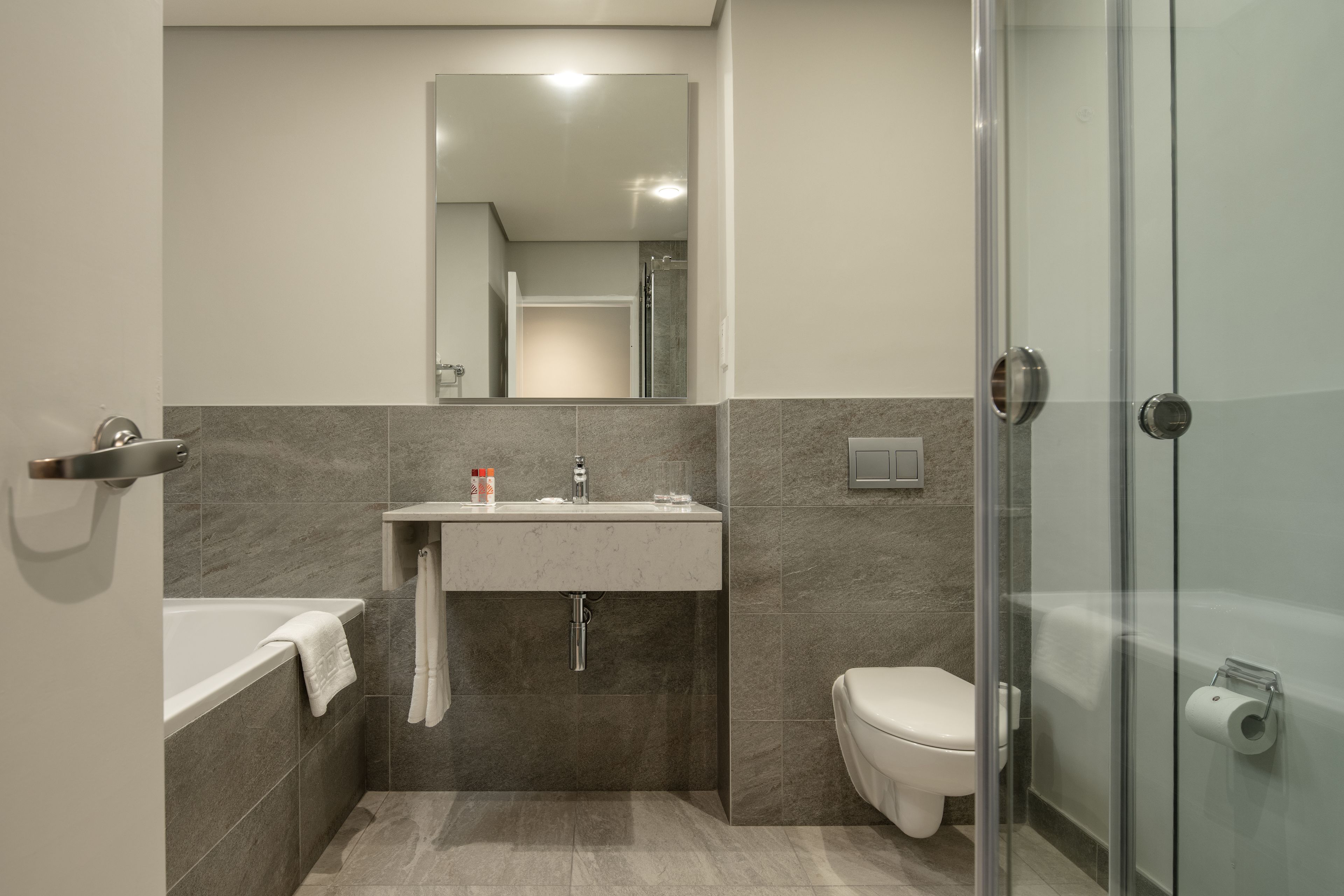 Un baño moderno con cabina de ducha de vidrio, inodoro blanco y lavabo con espejo superior.