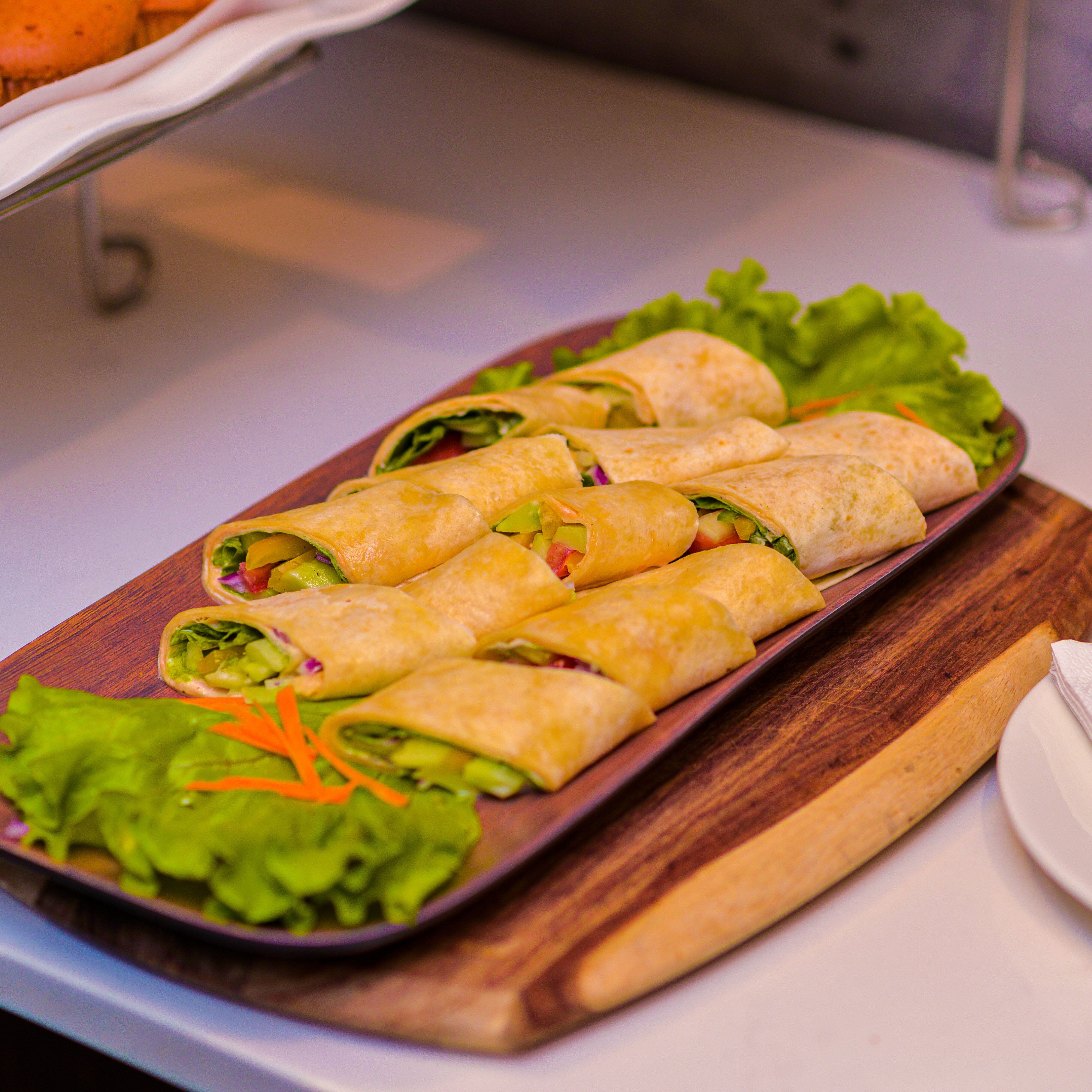 A tray of rolled sandwiches with lettuce and shredded carrots on a wooden board.
