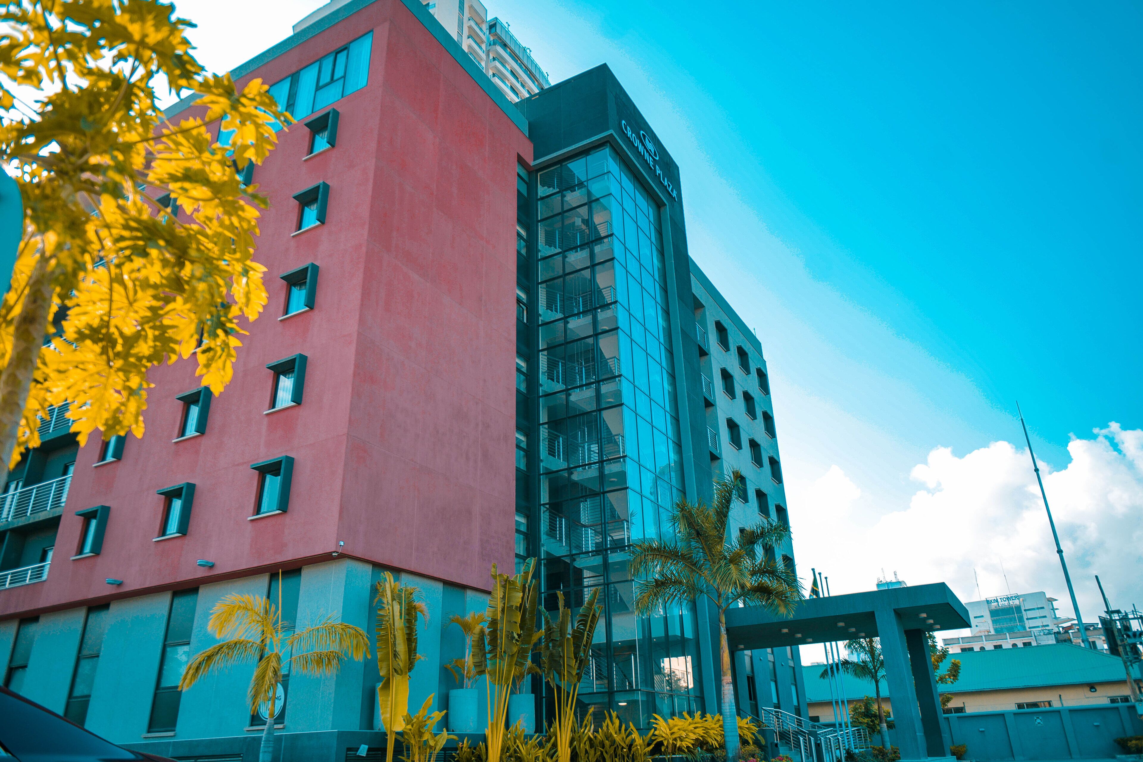 Un edificio moderno con fachada roja y sección de vidrio, con cielo despejado y algunas palmeras al frente.