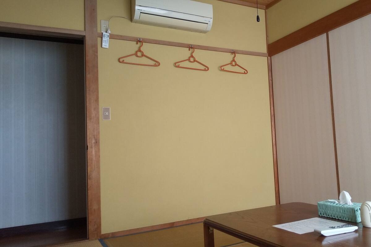 A room with a wooden table, a tissue box, and a remote control. There is a wooden wardrobe and a door with a hanging clothes rack.