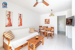 Un salon moderne et bien éclairé, avec un canapé en bois, une table à manger et des chaises, un ventilateur de plafond et des œuvres d’art accrochées aux murs.