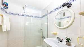 A bathroom with a glass-enclosed shower, a sink with a mirror, and decorative tiles. - Apartamentos el Rocio Casa Azahar (Alcala de Xivert)