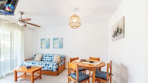 A modern living room with a sofa, dining table, chairs, ceiling fan, and pendant light. - Apartamentos el Rocio Casa Azahar (Alcala de Xivert)