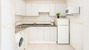 A compact kitchen with white cabinets, a built-in washing machine, a microwave, and a coffee maker. - Apartamentos el Rocio Casa Azahar (Alcala de Xivert)