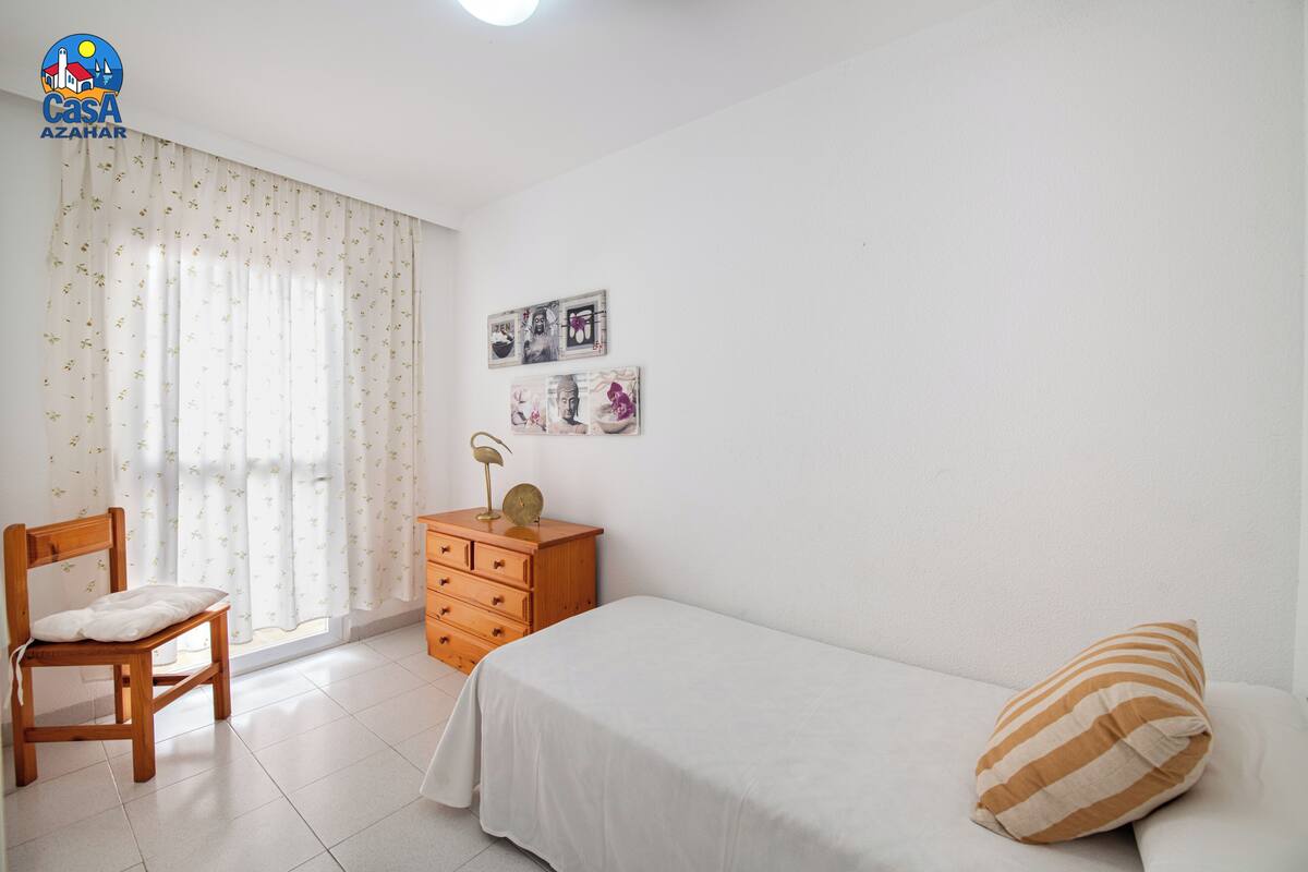 A bedroom with a bed, a chair, a dresser, and a window with curtains.