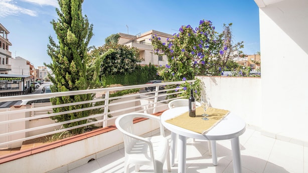 A balcony with white chairs and a table, a potted tree, and a view of the cityscape. - Apartamentos el Rocio Casa Azahar (Alcala de Xivert)