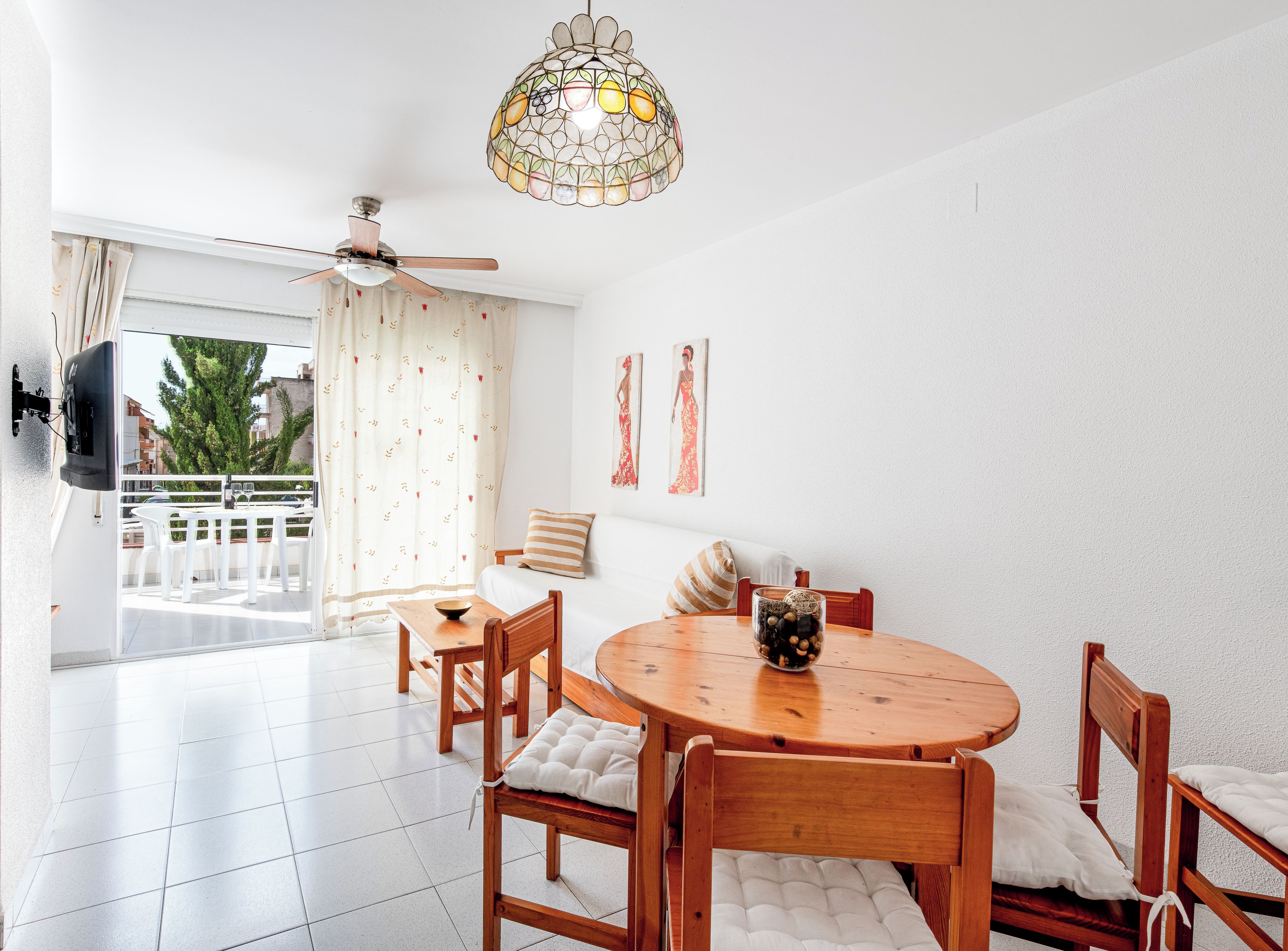 A modern dining area with a round wooden table, white cushioned chairs, and a ceiling fan.