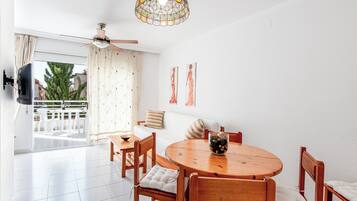 A modern dining area with a round wooden table, white cushioned chairs, and a ceiling fan.