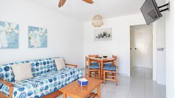 Une pièce comprenant un canapé en bois, une table en bois, un ventilateur de plafond, un téléviseur fixé au mur et deux tableaux accrochés au mur.