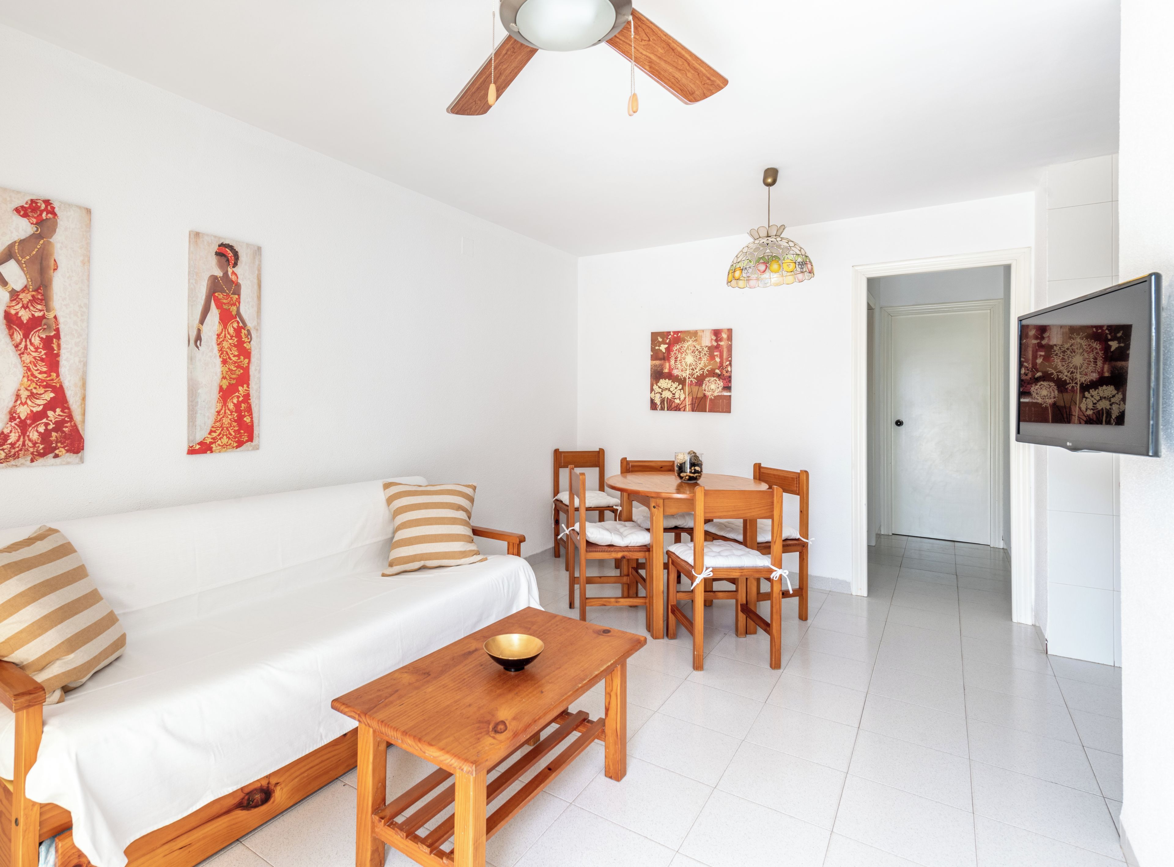 Un salon moderne et bien éclairé, avec un canapé en bois, une table à manger et des chaises, un ventilateur de plafond et des œuvres d’art accrochées aux murs.