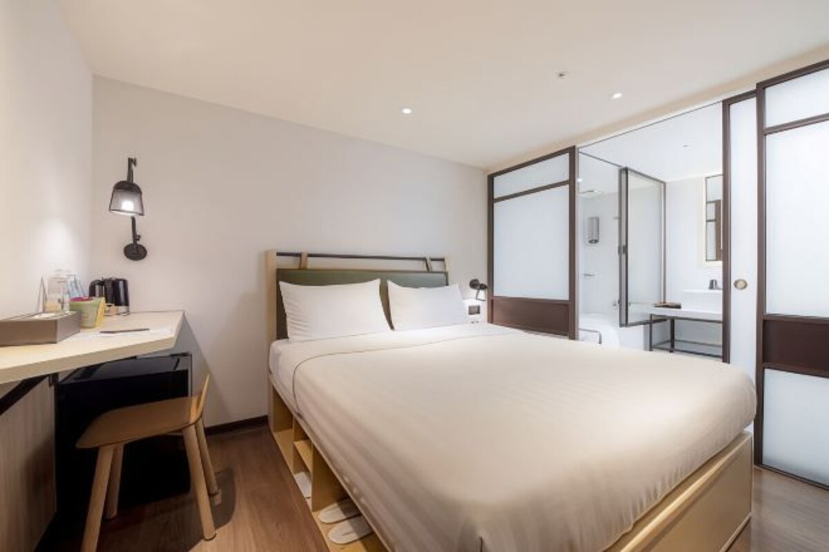A hotel room with a bed, desk, chair, lamp, and a sliding door leading to a bathroom.