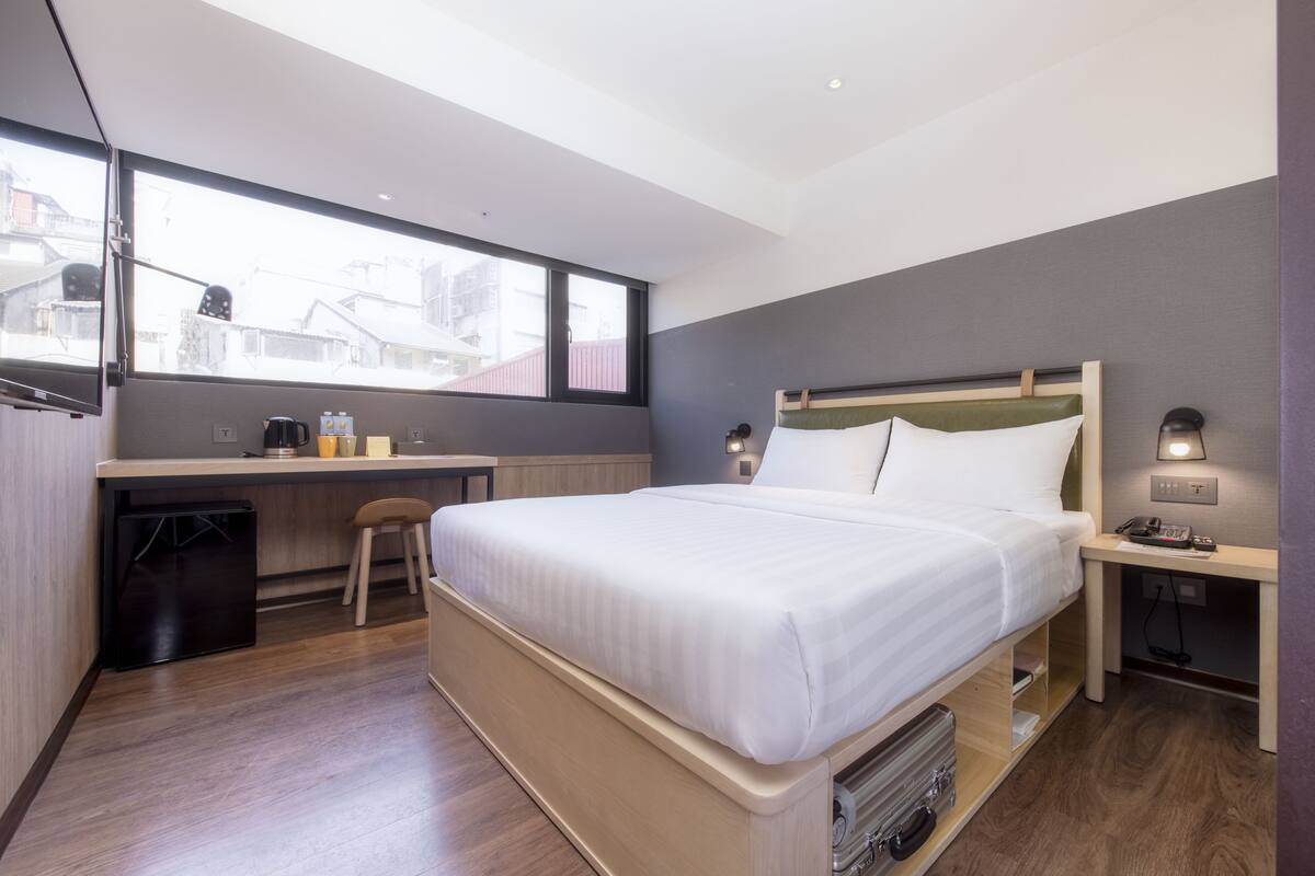 A modern hotel room with a large bed, a desk, and a chair.