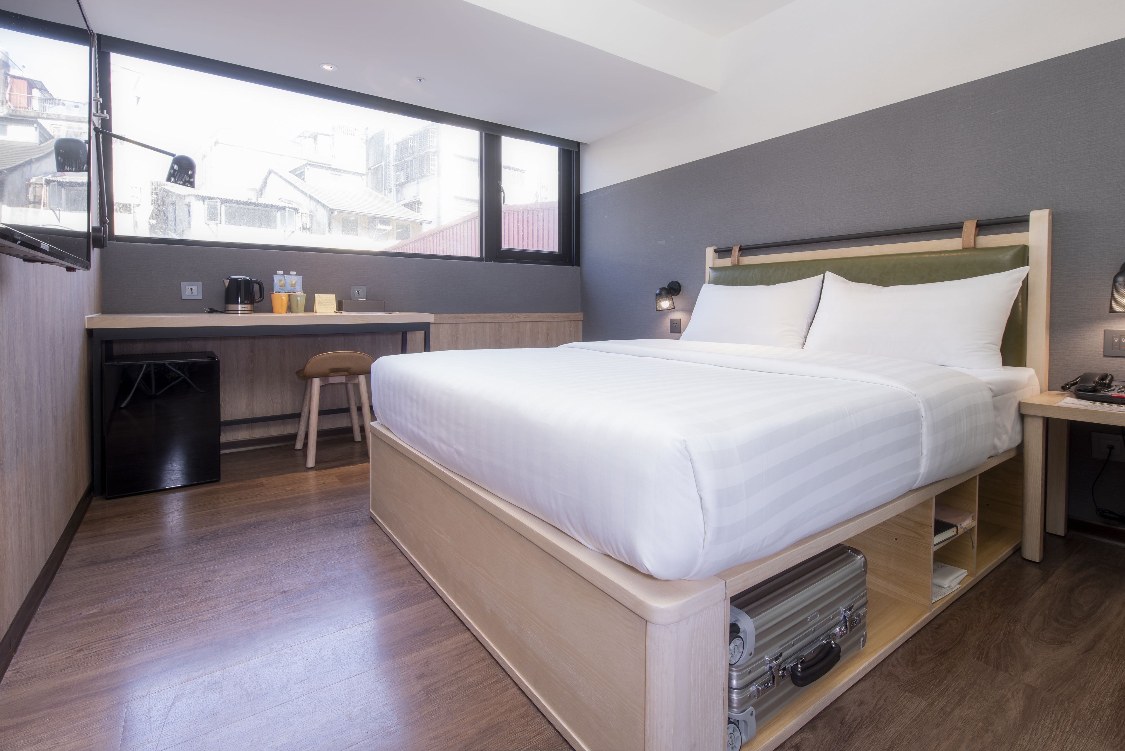A modern hotel room with a bed, desk, and a view of the city.