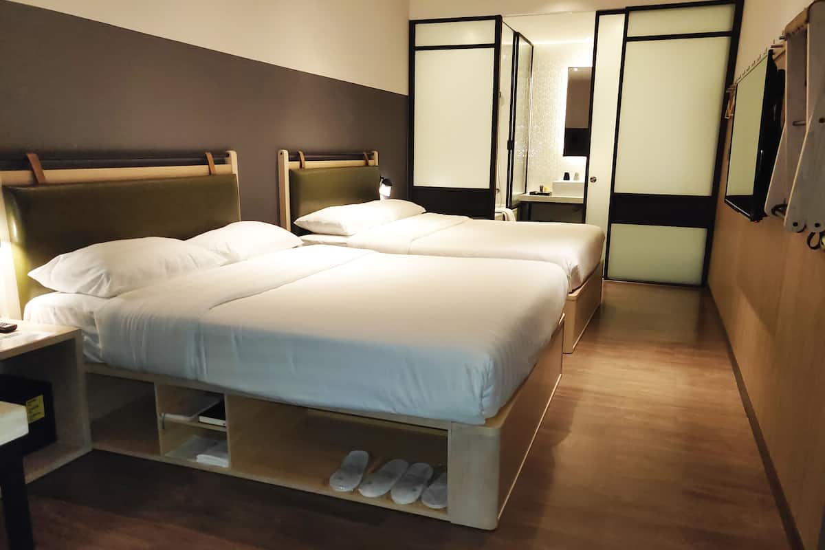 A hotel room with two beds, a nightstand, a mirror, and a shoe rack.