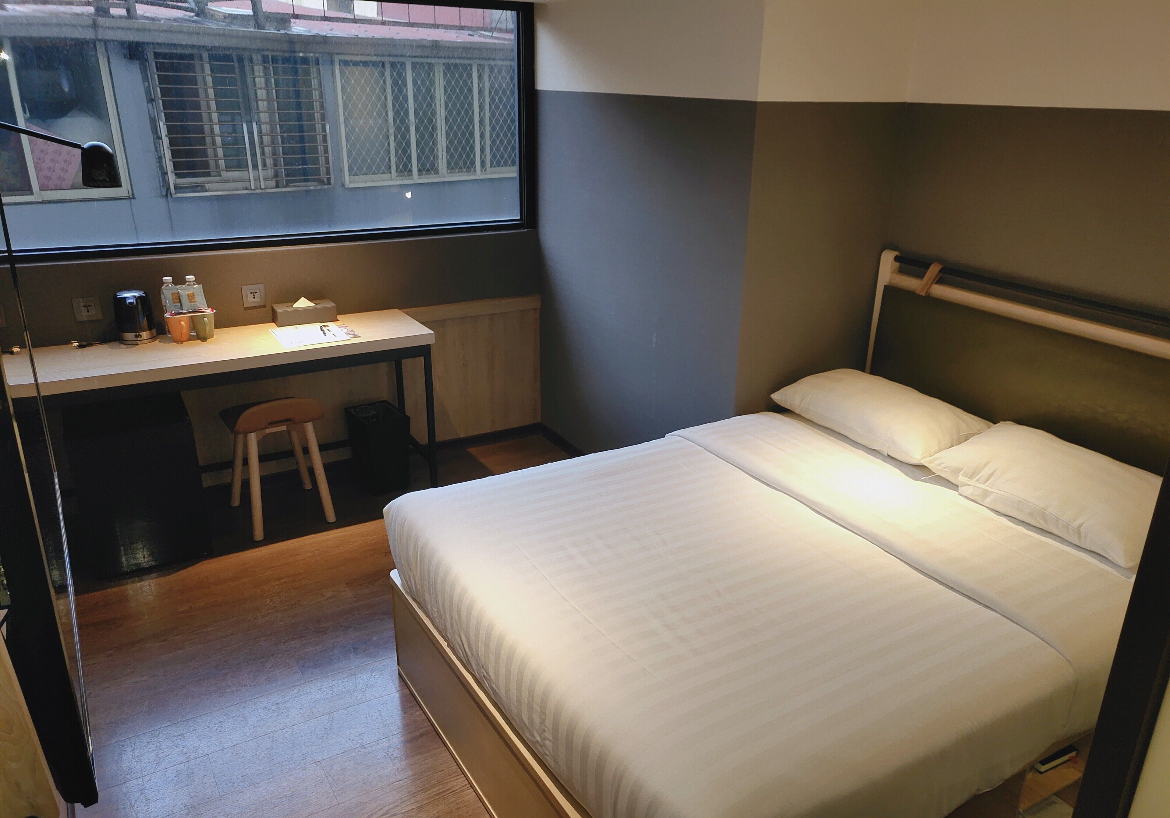 A hotel room with a bed, a desk, and a window.