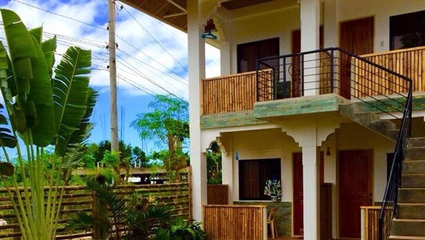 A two-story house with a balcony, a staircase, and a garden area with stepping stones. - John Verhel Homes and Island Tours (Panglao)