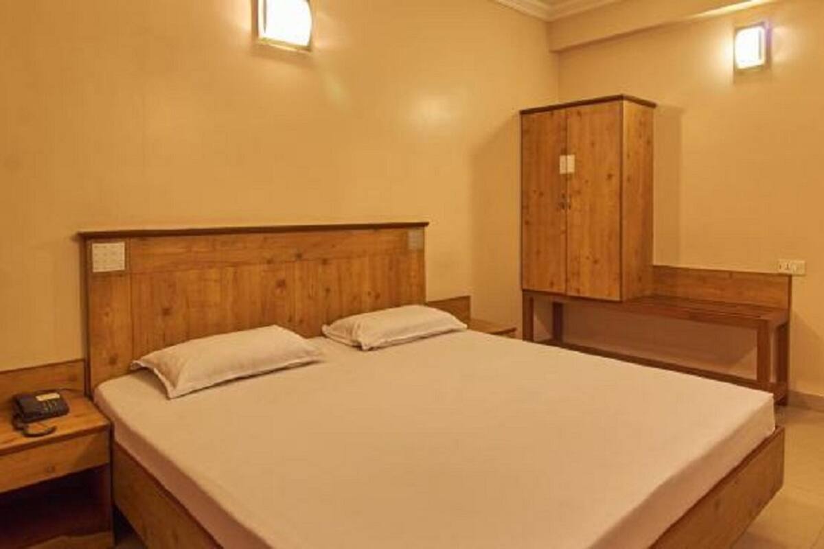 A bedroom with a wooden bed, a nightstand, a wooden wardrobe, and a wall-mounted light fixture.