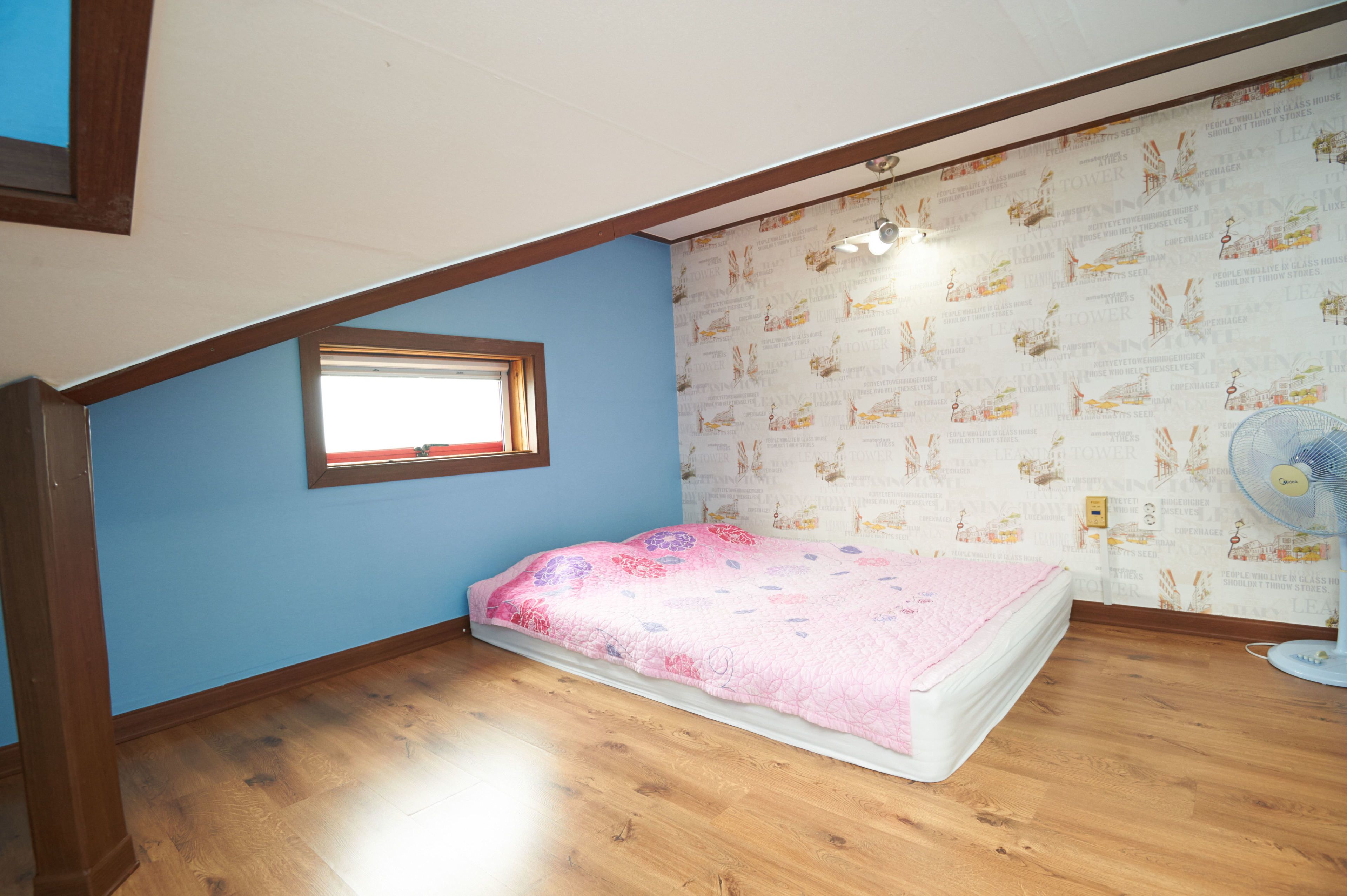 Un dormitorio con una cama individual, una ventana, un ventilador de pared y un papel tapiz estampado.