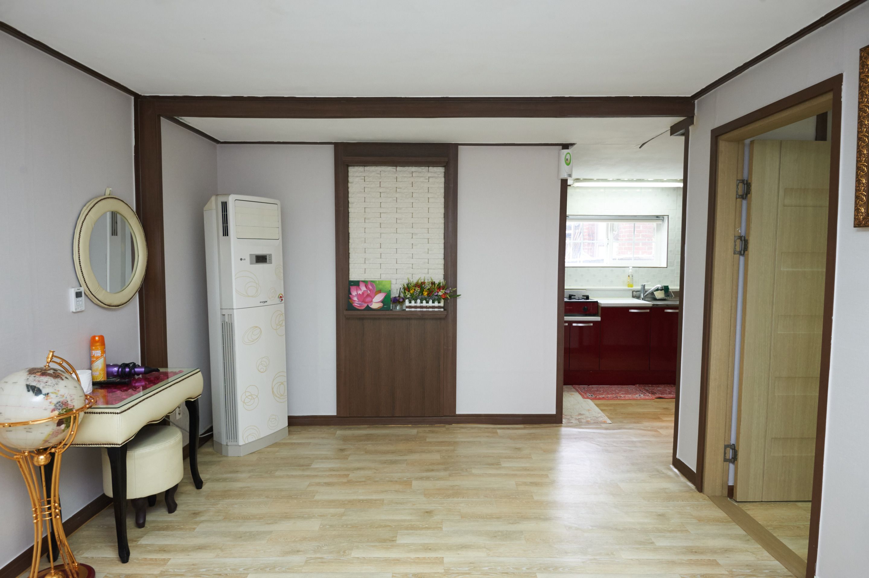 Una stanza con pavimento in legno, un frigorifero bianco, un tavolino con un mappamondo e uno specchio appeso al muro.