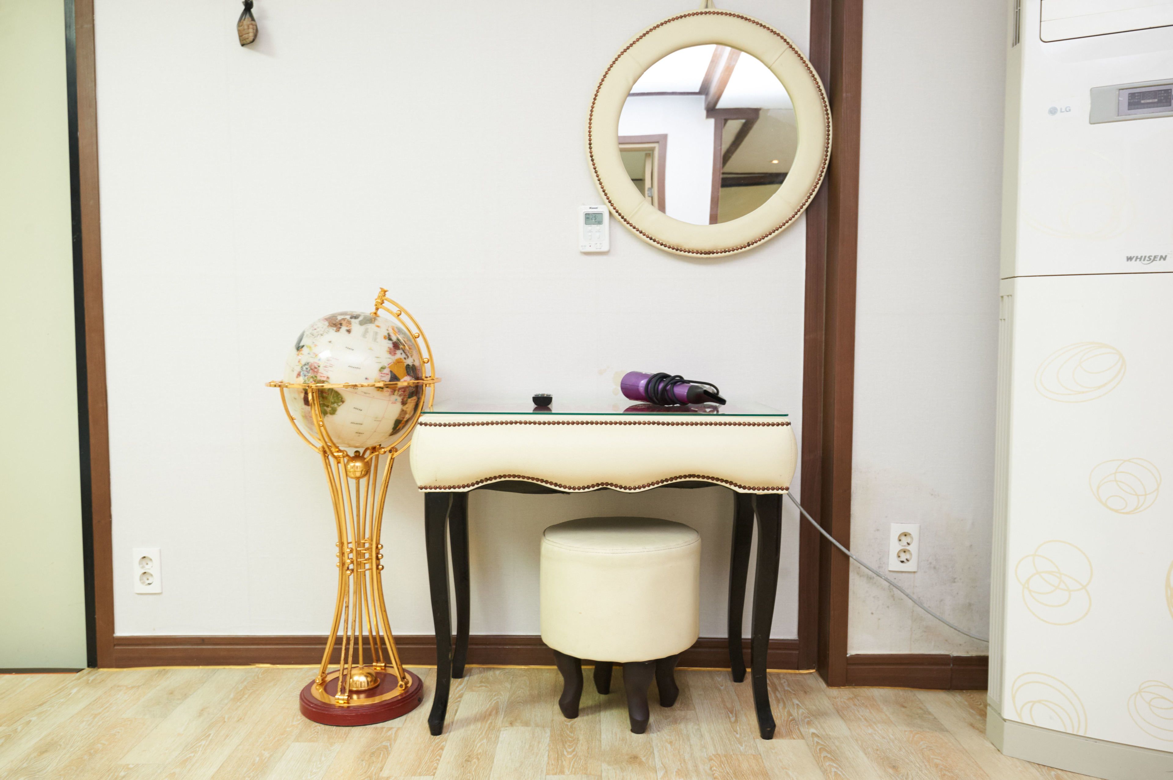 Una habitación con piso de madera, un escritorio blanco con espejo, un globo en un pedestal y un electrodoméstico blanco con un diseño circular.