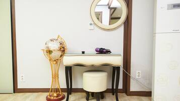 Una habitación con piso de madera, un escritorio blanco con espejo, un globo en un pedestal y un electrodoméstico blanco con un diseño circular.